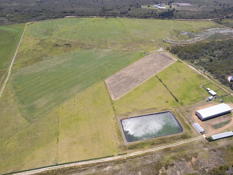 Aerial view of a large residential vacant land plot featuring a dam, agricultural fencing, and existing shed structures.
