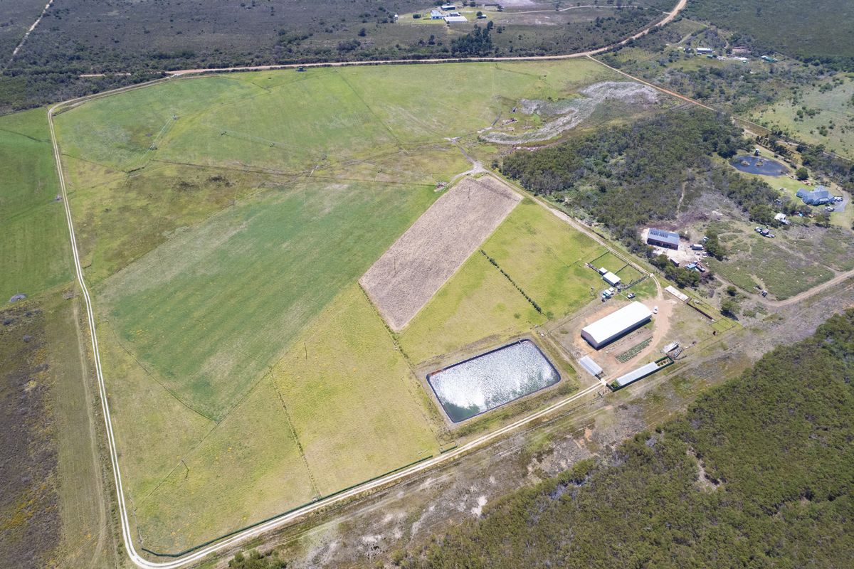 Aerial view of a large residential vacant land parcel featuring agricultural fencing, an irrigation dam, and existing outbuildings.