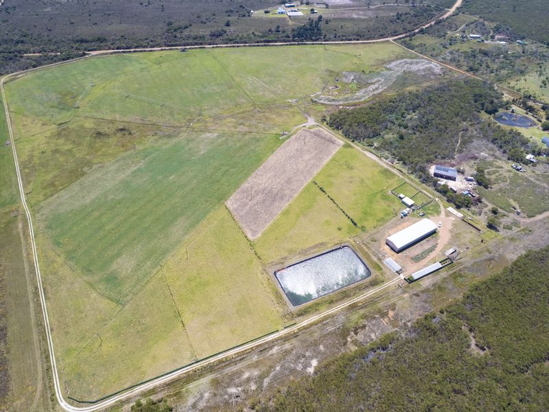 Aerial view of a large residential vacant land parcel featuring agricultural fencing, an irrigation dam, and existing outbuildings.