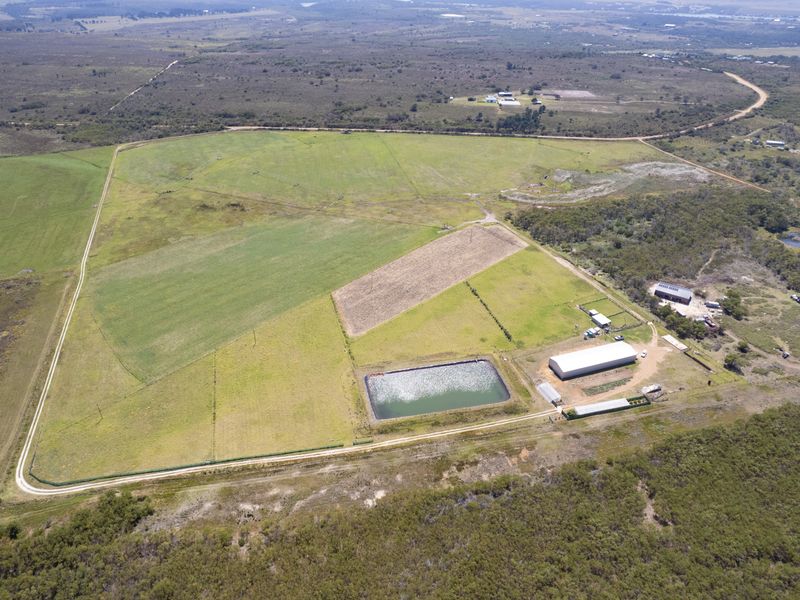 Aerial view of a large residential vacant land parcel featuring cleared pasture, a water storage dam, and existing metal shed infrastructure.