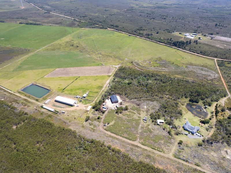 Aerial view of a large rural property featuring agricultural land, a farm dam, multiple outbuildings, and a residential dwelling.