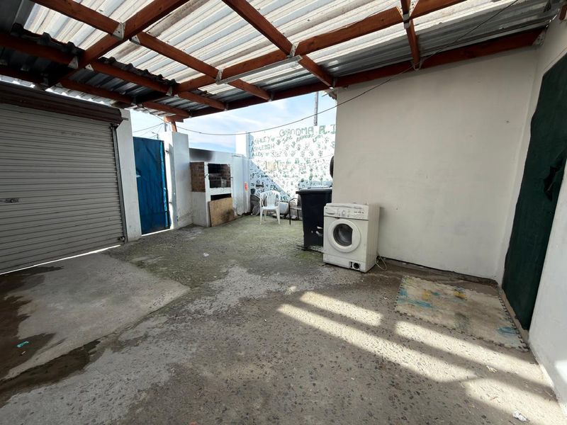 A covered outdoor patio area featuring a built-in brick braai, concrete flooring, and direct access to a garage.