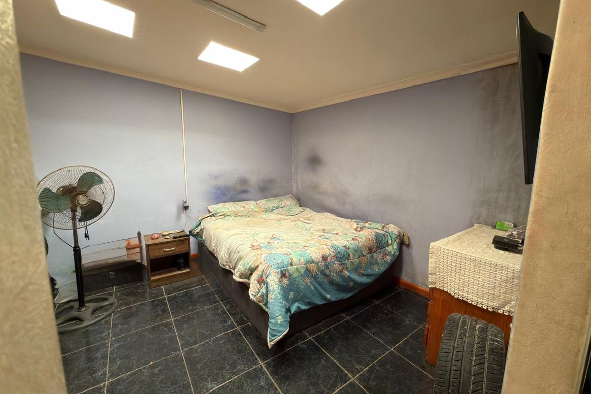 A bedroom featuring dark tiled flooring and recessed ceiling lighting, currently showing significant wall staining and surface wear requiring maintenance and cosmetic updates.