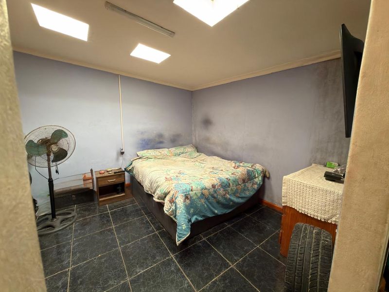A bedroom featuring dark tiled flooring and recessed ceiling lighting, currently showing significant wall staining and surface wear requiring maintenance and cosmetic updates.