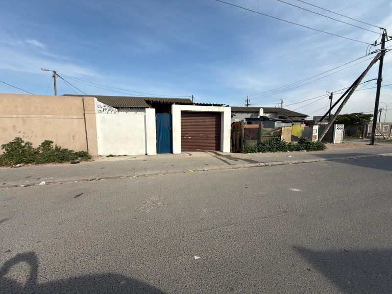 Street view of a townhouse property featuring a roller shutter garage door and boundary wall with visible signs of wear and weathering.