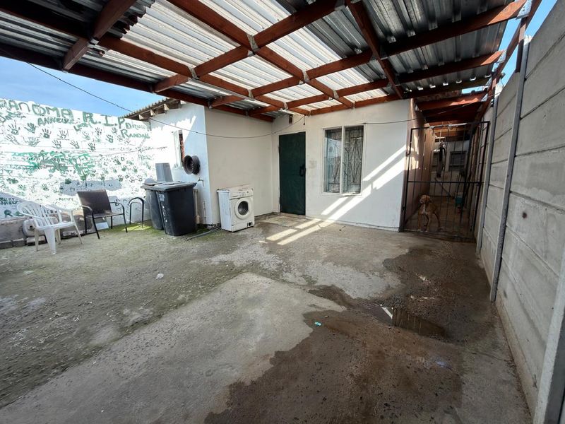 A covered outdoor patio area featuring a timber roof structure, concrete flooring, and a secure gated side access point.