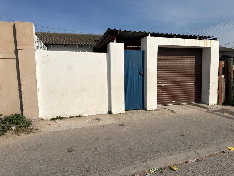 Front exterior view of the townhouse featuring a roller garage door, pedestrian gate, and boundary wall with visible signs of wear and weathering.
