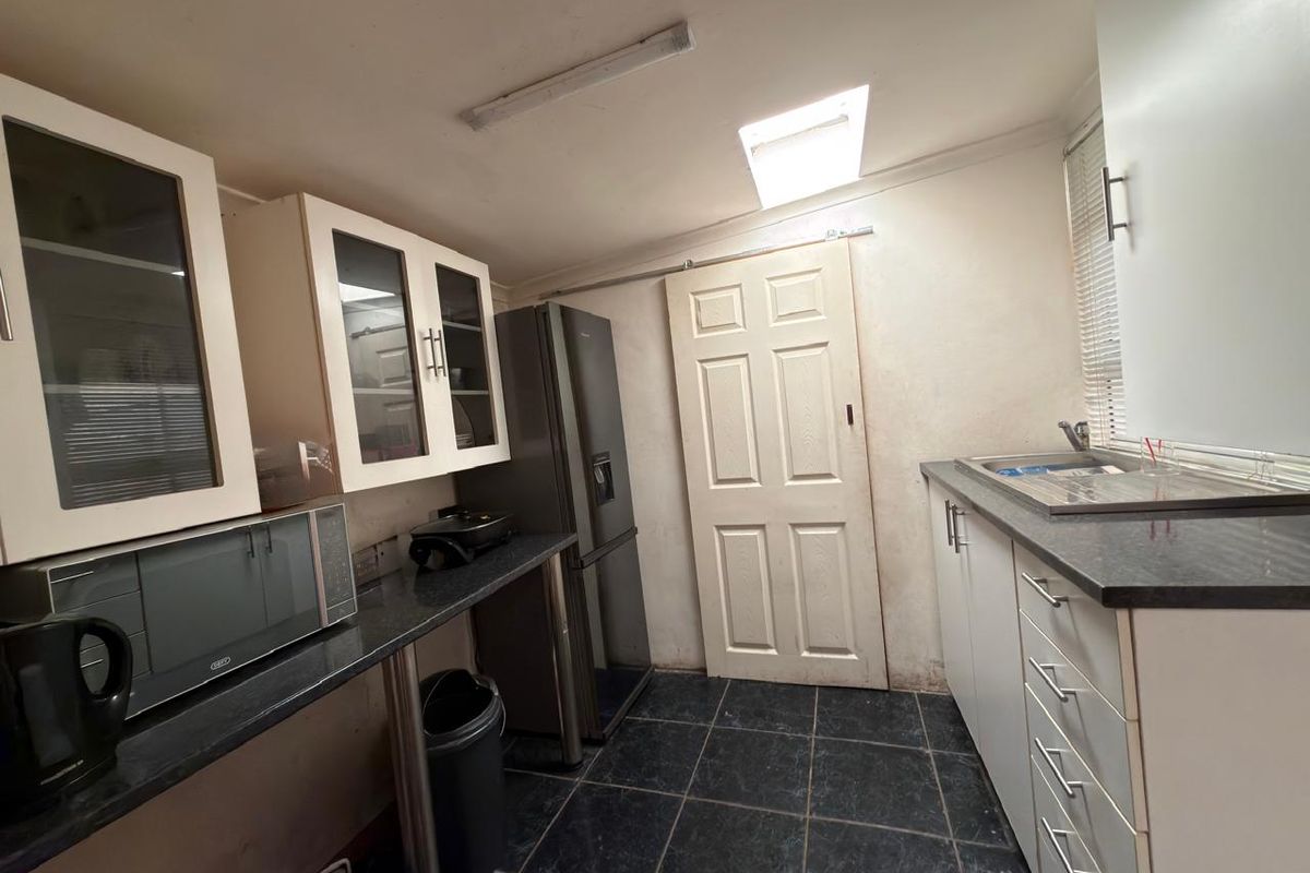 A functional scullery featuring built-in cabinetry, dark laminate countertops, a stainless steel sink, and a skylight for natural illumination.