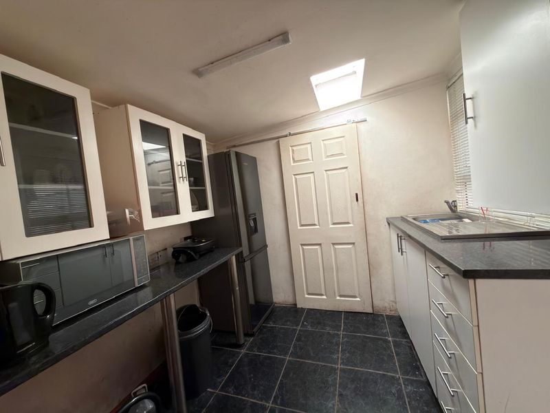 A functional scullery featuring built-in cabinetry, dark laminate countertops, a stainless steel sink, and a skylight for natural illumination.