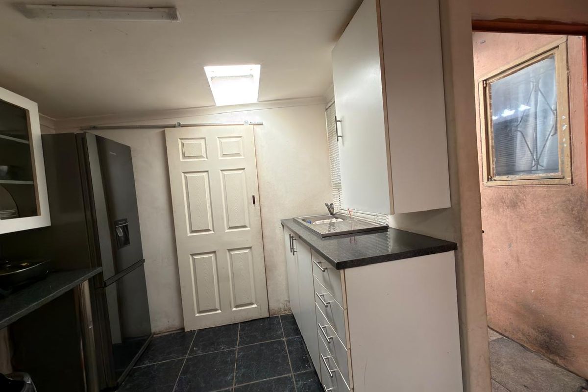 A functional scullery area featuring built-in cabinetry, dark laminate countertops, a stainless steel sink, and tiled flooring with natural light from a skylight.