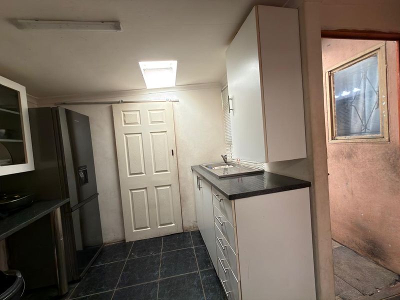 A functional scullery area featuring built-in cabinetry, dark laminate countertops, a stainless steel sink, and tiled flooring with natural light from a skylight.
