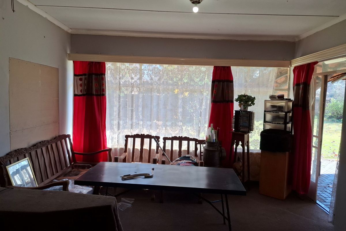 A living room featuring a large picture window and sliding door access to the garden, requiring cosmetic updates to the walls and flooring.