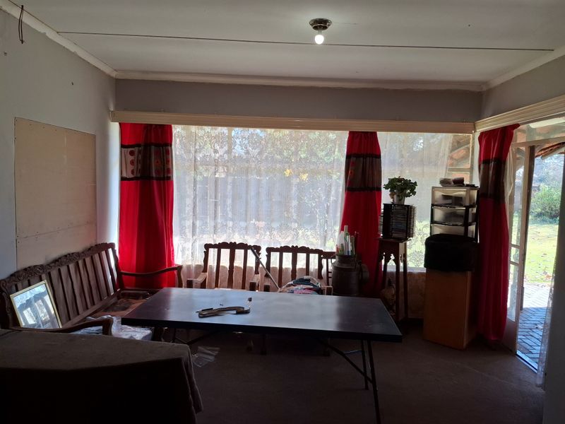 A living room featuring a large picture window and sliding door access to the garden, requiring cosmetic updates to the walls and flooring.