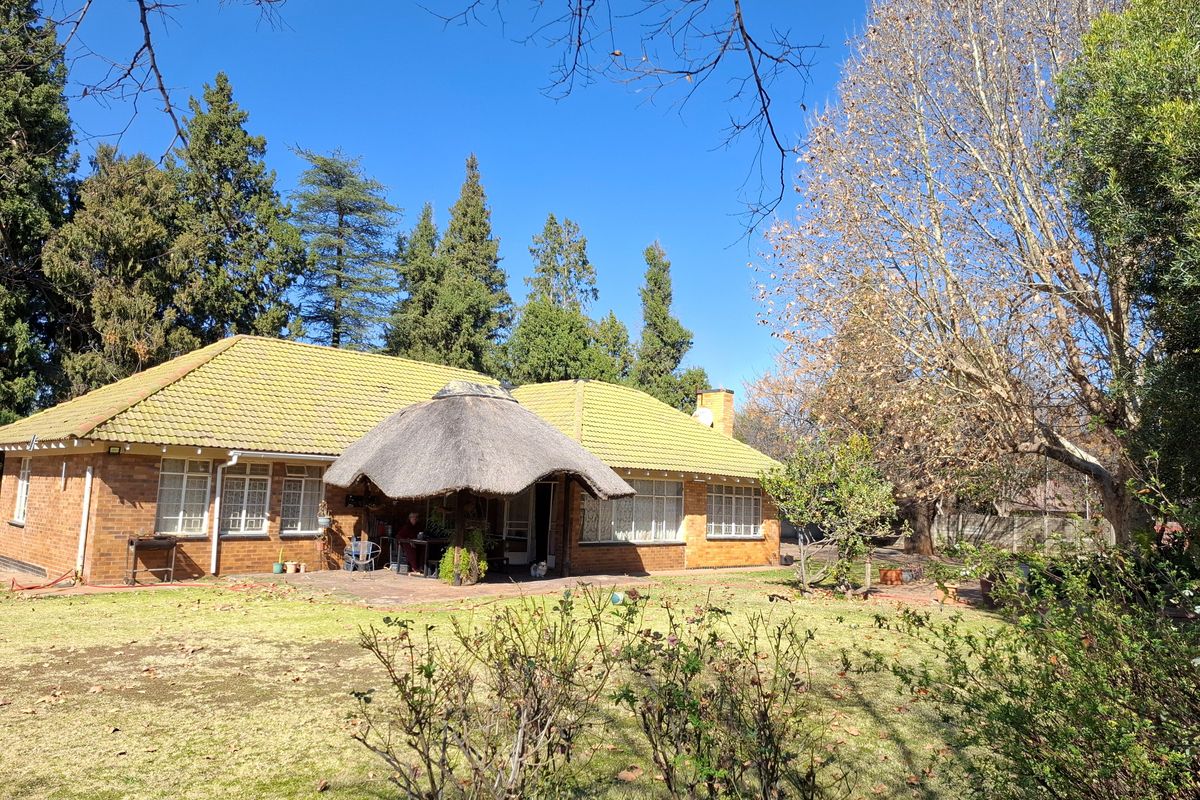 Rear view of a brick house featuring a tiled roof, a thatched lapa over a paved patio, and a spacious garden area.