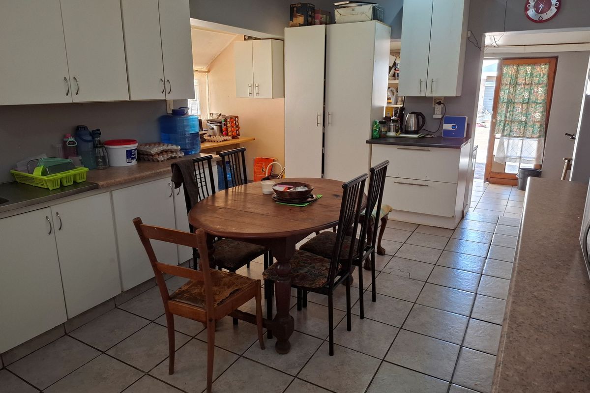 A functional kitchen featuring white cabinetry, laminate countertops, and tiled flooring, with direct access to the rear exterior through a glass-panelled door.