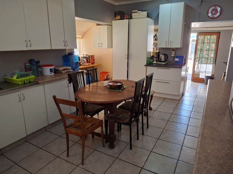 A functional kitchen featuring white cabinetry, laminate countertops, and tiled flooring, with direct access to the rear exterior through a glass-panelled door.