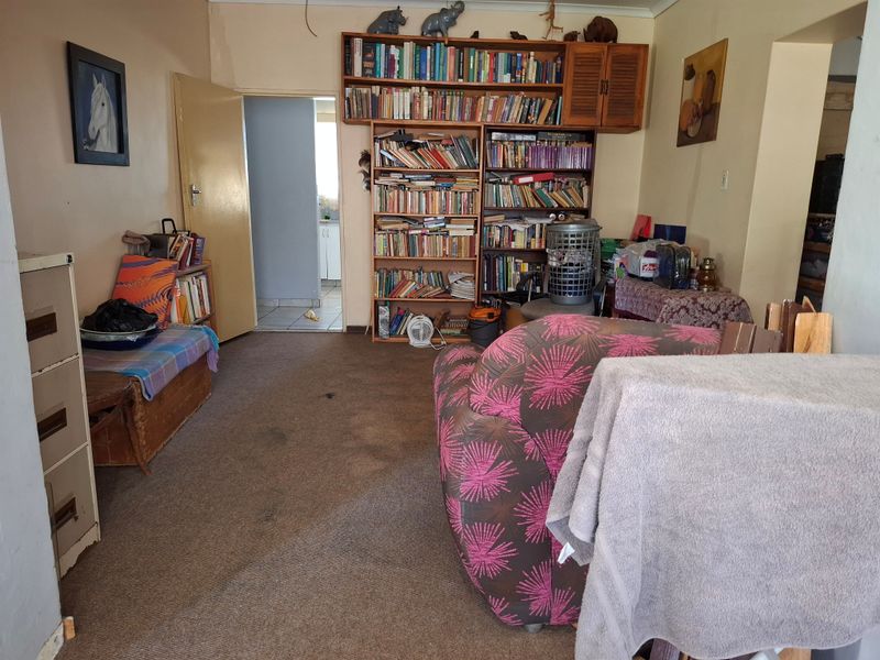 A living room featuring a large built-in wooden shelving unit and carpeted flooring, providing a functional space with potential for modernization.