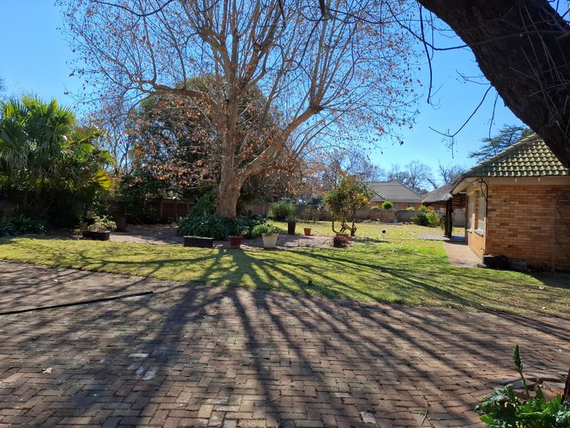 Spacious rear garden featuring mature trees, established lawn, and extensive brick paved areas adjacent to the brick-built house.