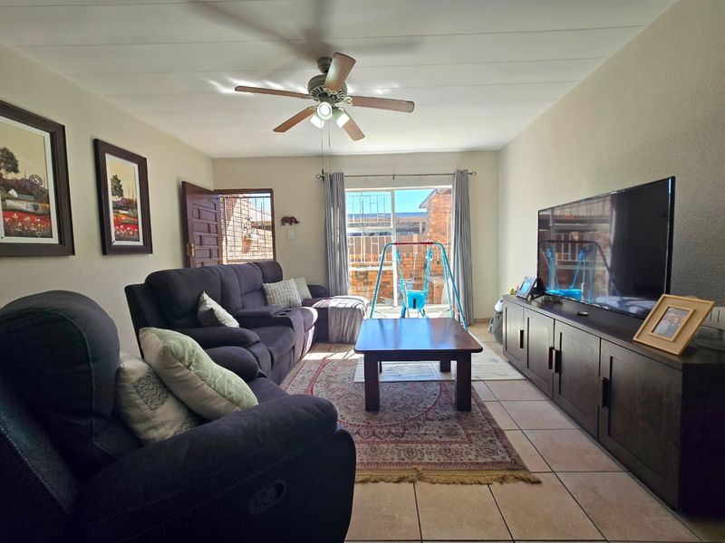 A comfortable living room featuring tiled flooring, a ceiling fan, and a sliding door providing access to the outdoor area.
