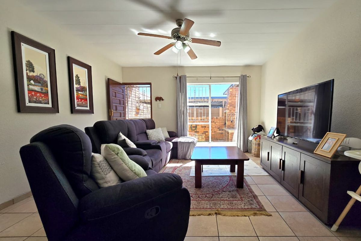 A comfortable living room featuring tiled flooring, a ceiling fan, and a sliding glass door providing access to the outdoor area.