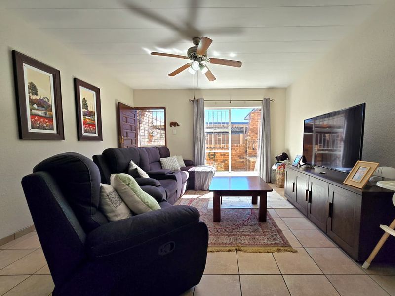 A comfortable living room featuring tiled flooring, a ceiling fan, and a sliding glass door providing access to the outdoor area.