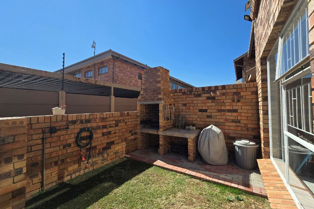 Private rear courtyard featuring a built-in brick braai, paved patio area, and a small lawn, perfect for outdoor entertaining.