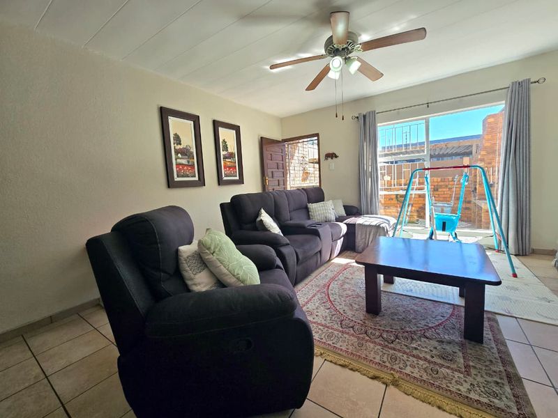 A comfortable living room featuring tiled flooring, a ceiling fan, and a sliding glass door providing access to the outdoor area.