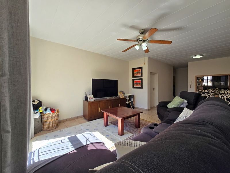 A comfortable living room featuring tiled flooring, a panelled ceiling, and a ceiling fan, providing a functional and well-lit space for relaxation.