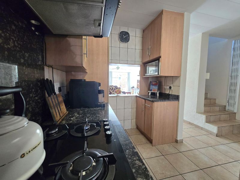 A functional kitchen featuring granite countertops, a gas hob with extractor fan, and built-in cabinetry, with tiled flooring and a view into the living area.