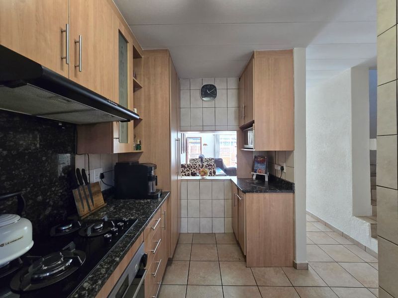 A functional kitchen featuring light wood cabinetry, granite countertops, a gas hob with extractor fan, and tiled flooring, with a pass-through window to the living area.