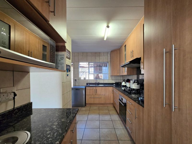 A functional galley-style kitchen featuring wood-finish cabinetry, granite countertops, a gas hob, and tiled flooring, offering ample storage and workspace.