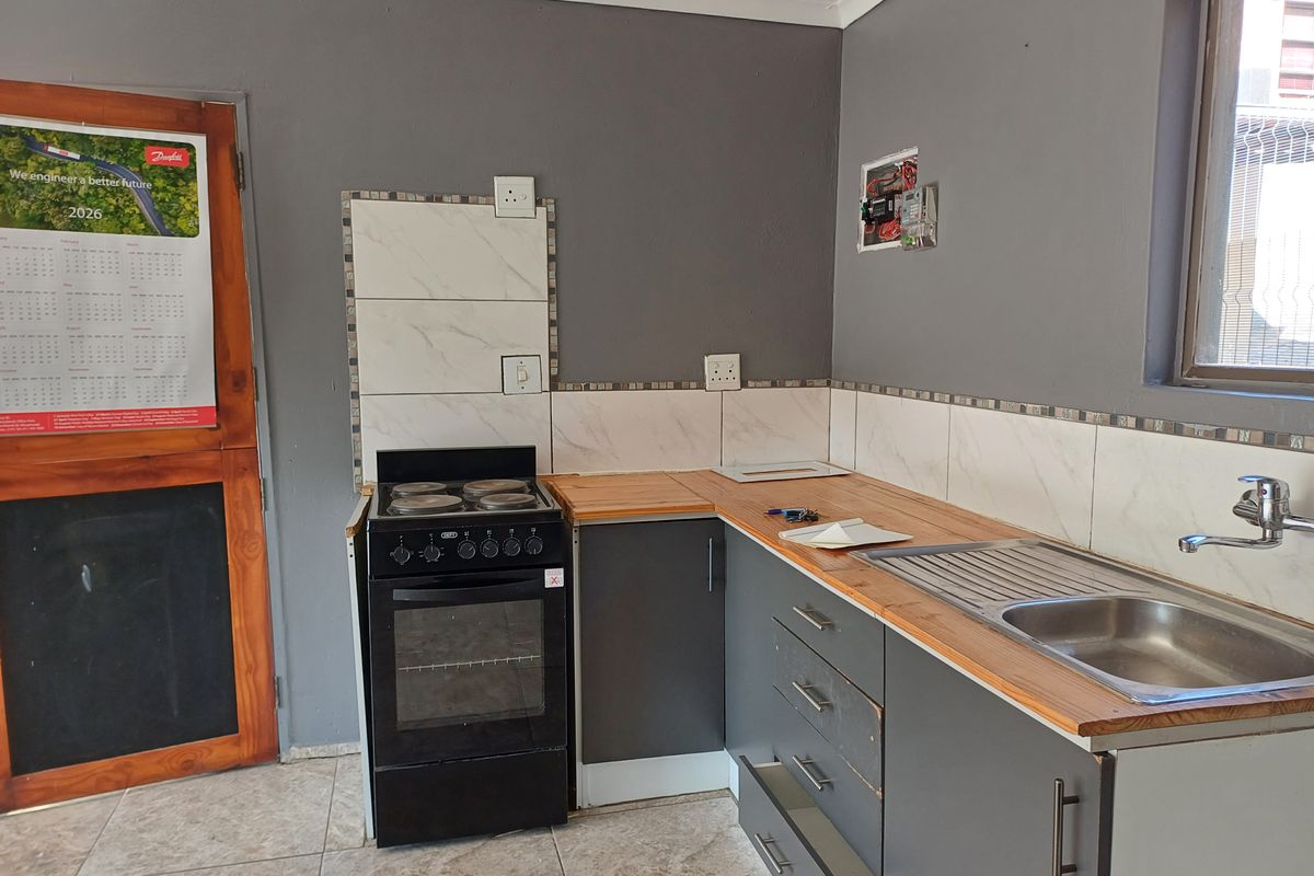 A compact kitchen featuring grey cabinetry, wooden countertops, a stainless steel sink, and a freestanding stove, requiring minor repairs and finishing touches.
