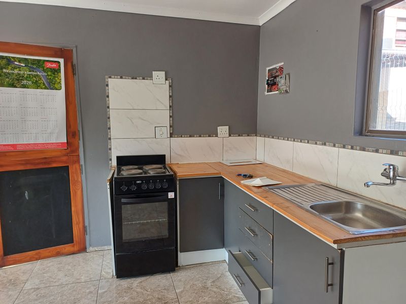A compact kitchen featuring grey cabinetry, wooden countertops, a stainless steel sink, and a freestanding stove, requiring minor repairs and finishing touches.
