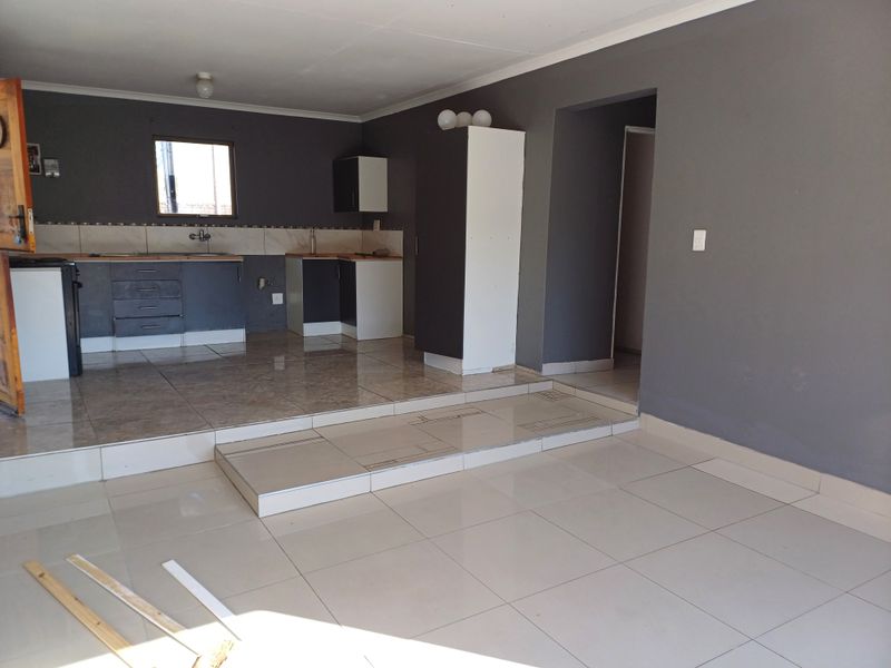 Open plan living and kitchen area featuring tiled flooring, a raised platform, and dark grey cabinetry, offering a blank canvas for interior design.