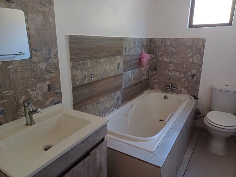 A functional bathroom featuring a built-in vanity with basin, a standard bathtub, and a toilet with decorative tiled wall accents.