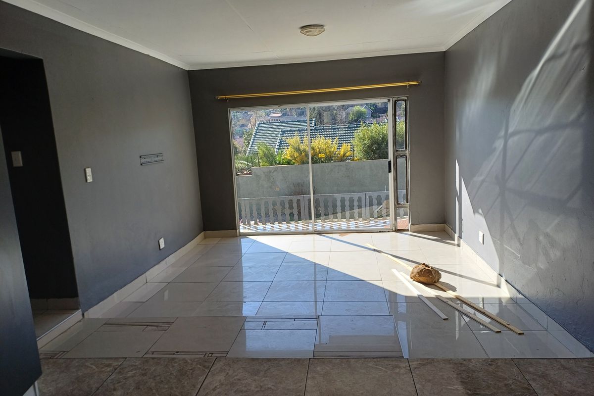 An empty living room featuring tiled flooring, grey painted walls, and a large sliding glass door providing access to the exterior.