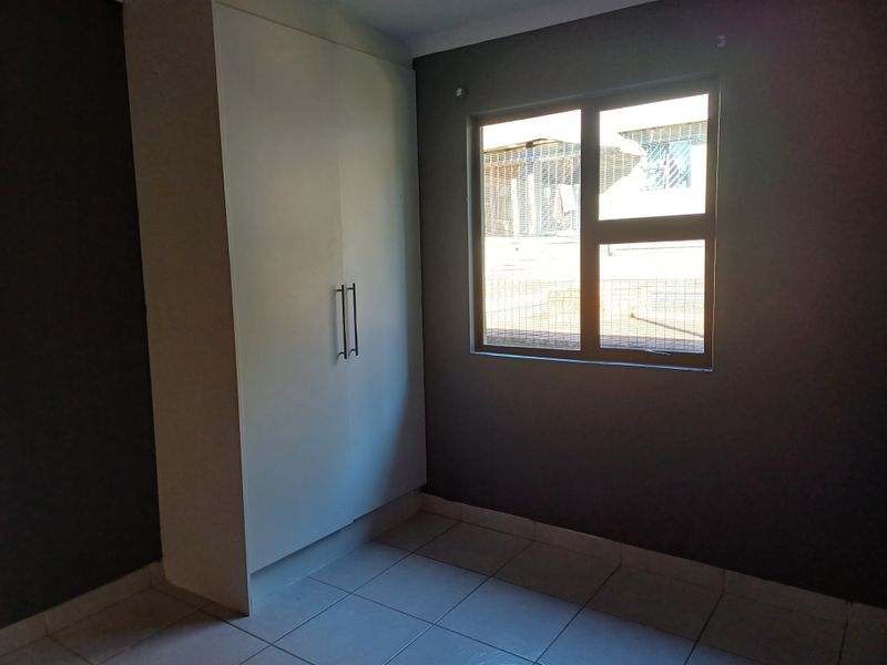 A clean, empty bedroom featuring tiled flooring, a built-in wardrobe, and a window with an aluminium frame.