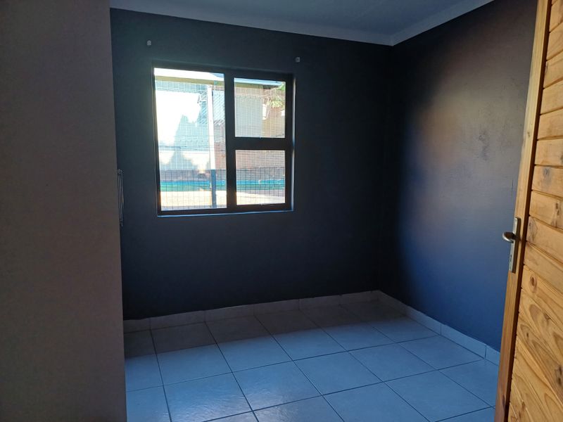 An empty bedroom featuring dark painted walls, tiled flooring, and an aluminium window frame, providing a blank canvas for personalization.