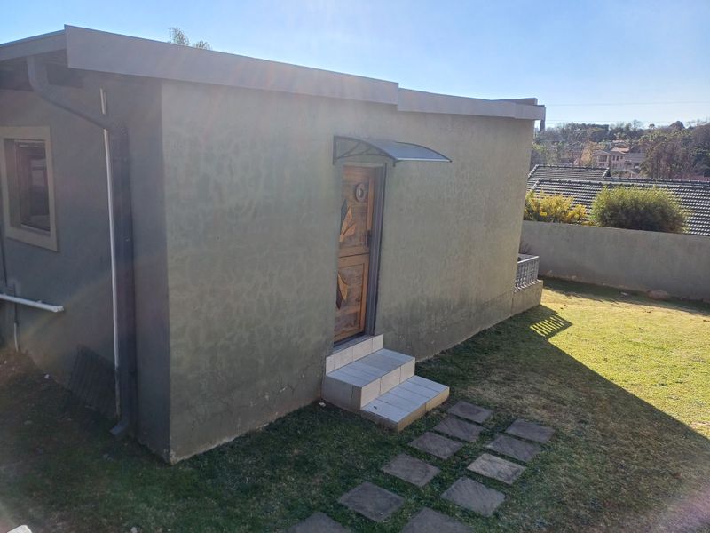Rear exterior view of the property featuring a side entrance with a small awning, tiled steps, and stone pavers leading into the garden area.