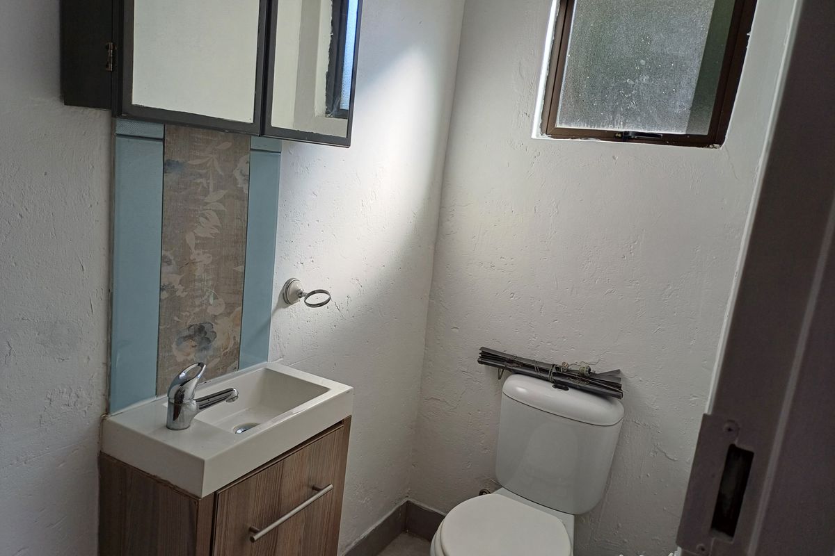 A compact bathroom featuring a vanity with basin, toilet, and medicine cabinet, requiring some cosmetic updates to the wall finishes.