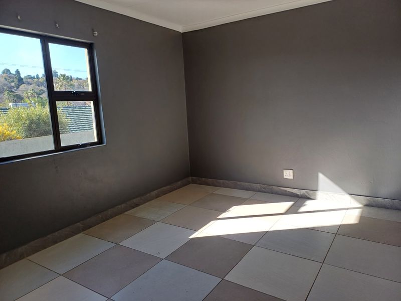 An empty bedroom featuring neutral tiled flooring, dark grey painted walls, and an aluminium-framed window providing natural light.