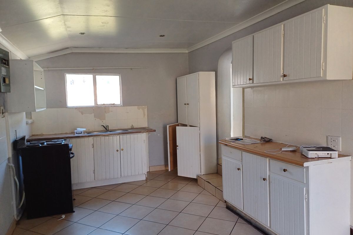 A dated kitchen featuring white cabinetry, tiled splashbacks, and tiled flooring, requiring cosmetic updates and repairs to the wall surfaces.