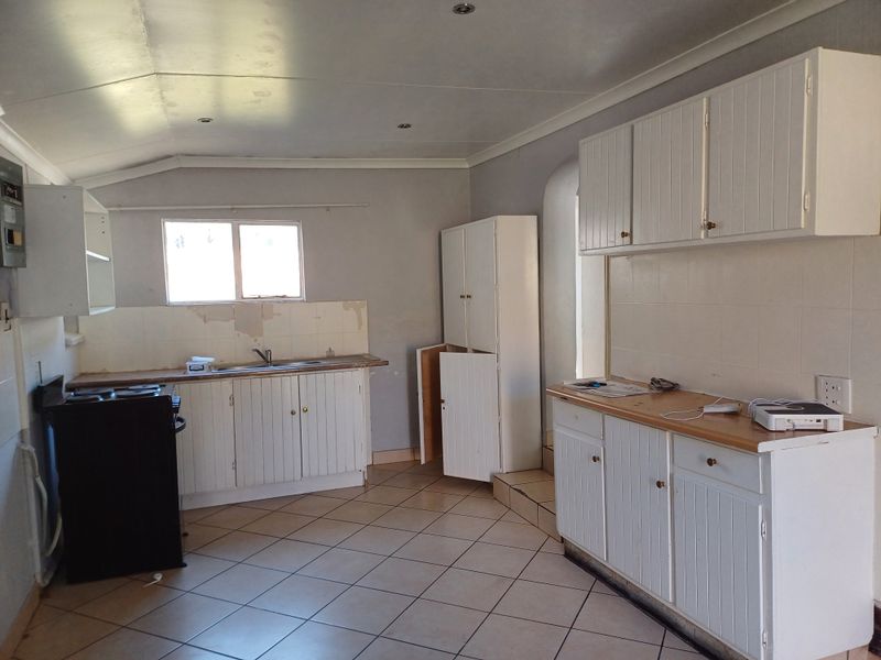 A dated kitchen featuring white cabinetry, tiled splashbacks, and tiled flooring, requiring cosmetic updates and repairs to the wall surfaces.