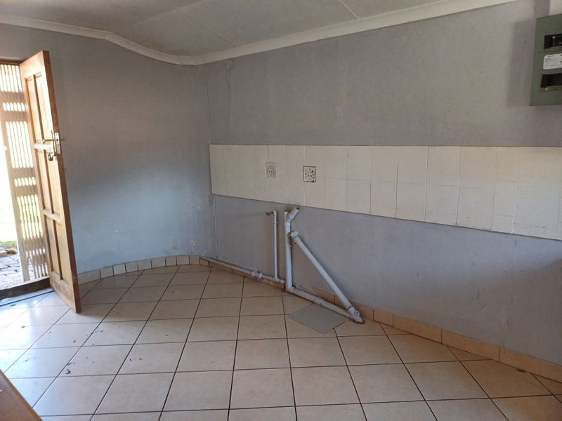 A functional laundry area featuring tiled flooring, a tiled splashback, and exposed plumbing connections, ready for appliance installation.