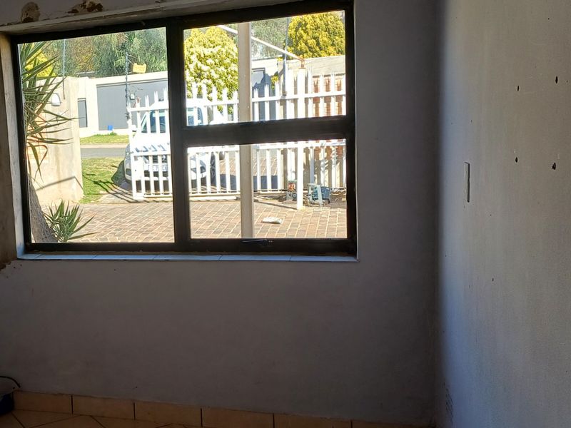 An empty living room space featuring tiled flooring and a large window, currently requiring cosmetic repairs to the surrounding wall plaster and paintwork.
