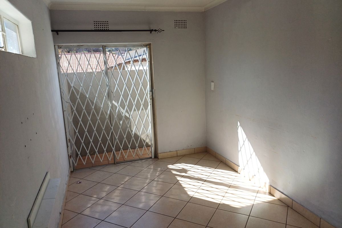 An empty living area featuring tiled flooring, a sliding glass door with a security gate, and neutral wall finishes.