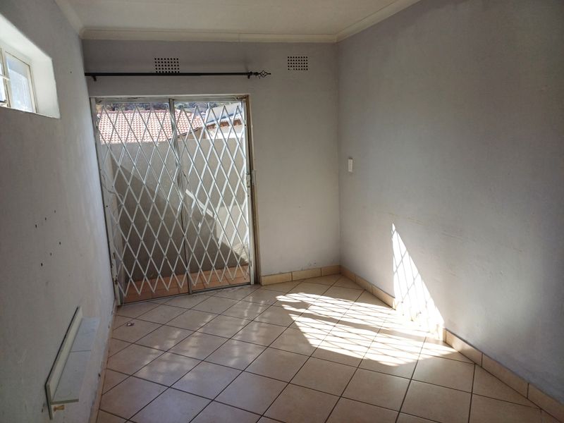 An empty living area featuring tiled flooring, a sliding glass door with a security gate, and neutral wall finishes.