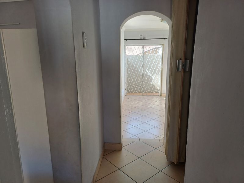 A tiled hallway featuring an arched doorway leading to an adjacent room with a security gate and sliding door access.