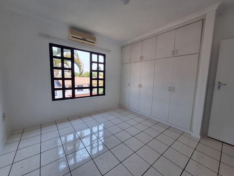 An empty bedroom featuring tiled flooring, built-in cupboards, and an air conditioning unit, offering a clean and functional space.