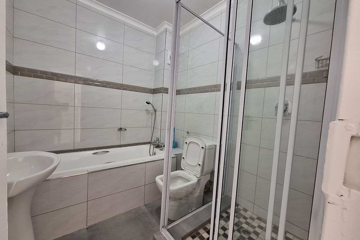 A modern, well-maintained bathroom featuring a separate bathtub, glass-enclosed shower, pedestal basin, and toilet with neutral wall and floor tiling.
